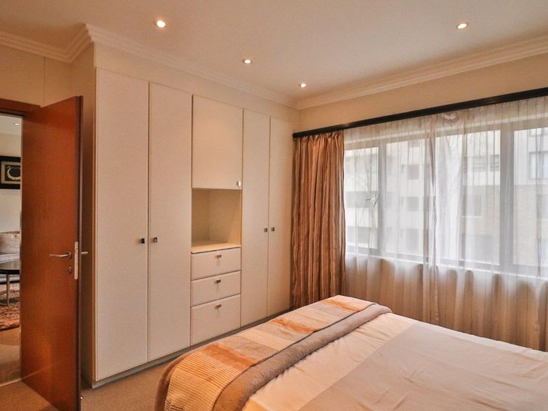 A well-maintained bedroom featuring extensive built-in cabinetry, recessed ceiling lighting, and large windows allowing for natural light.