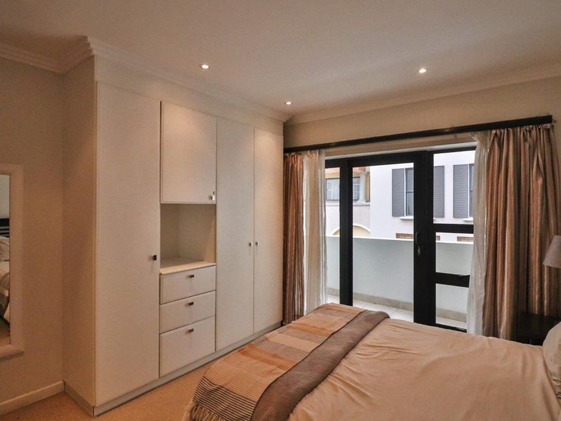 A well-maintained bedroom featuring built-in cupboards, recessed downlighting, and a sliding glass door providing access to a private balcony.