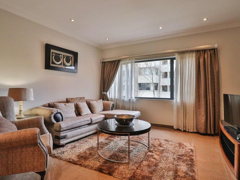 A well-maintained living room featuring tiled flooring, recessed downlighting, and large windows with neutral curtains, creating a comfortable and inviting atmosphere.