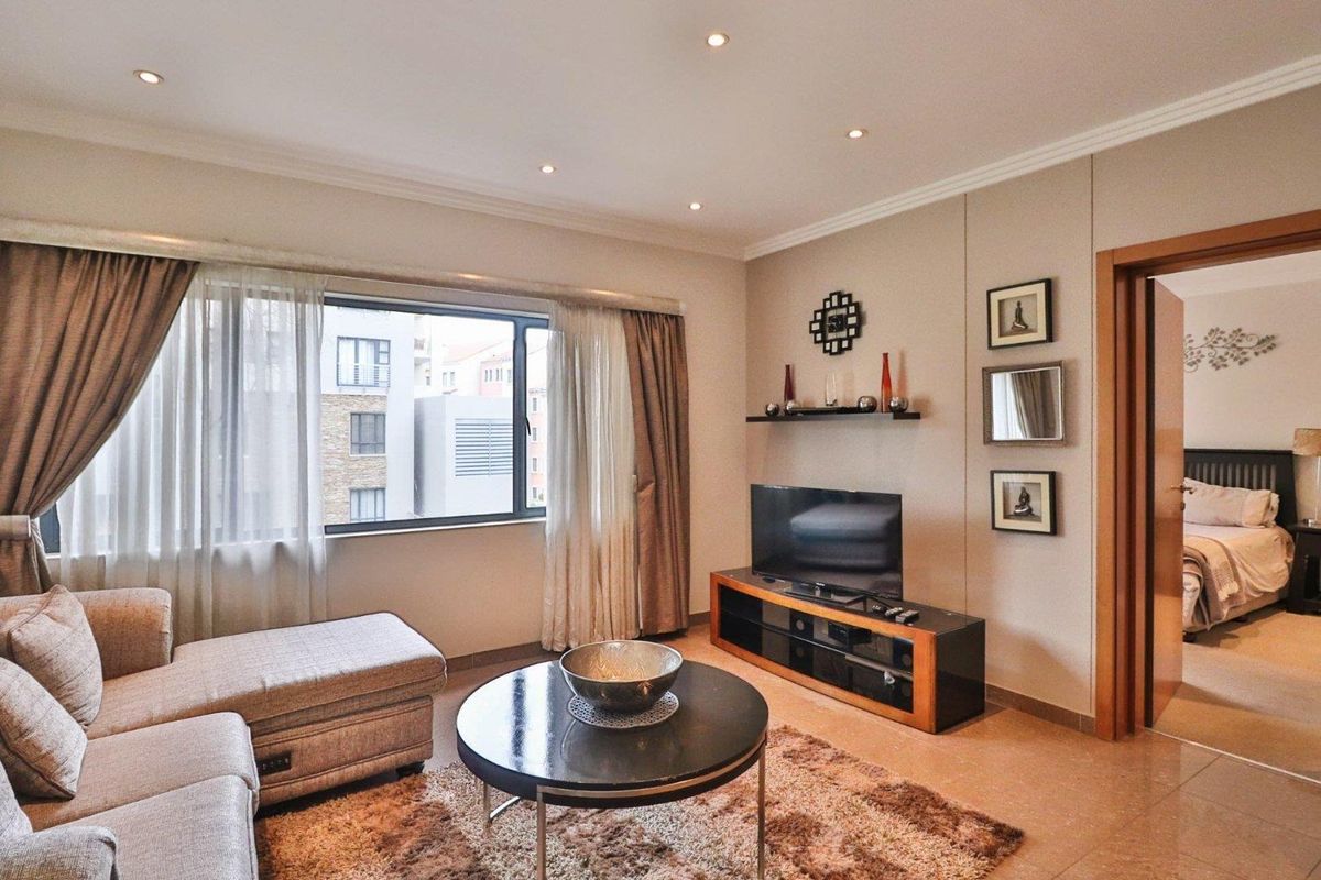 A well-maintained living room featuring tiled flooring, recessed downlighting, and a large window with neutral curtains, offering a comfortable and bright living space.