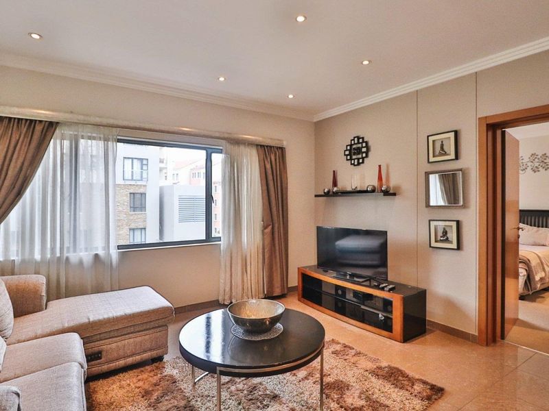A well-maintained living room featuring tiled flooring, recessed downlighting, and a large window with neutral curtains, offering a comfortable and bright living space.