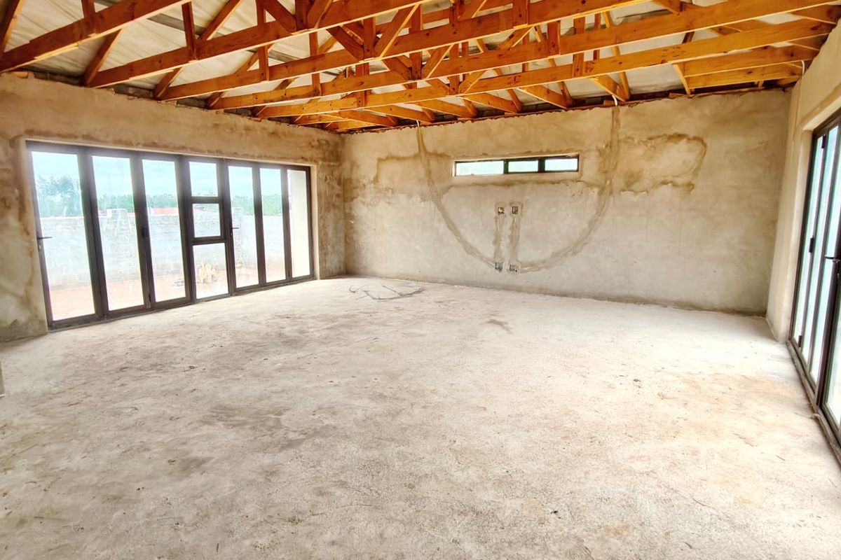Spacious open-plan living area in shell condition, featuring exposed timber roof trusses, concrete flooring, and large aluminium stacker doors providing ample natural light.