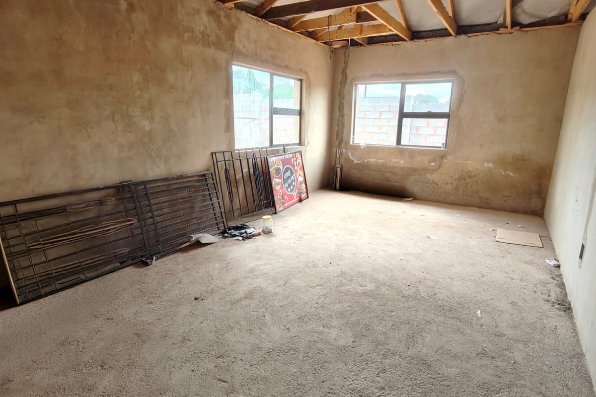 An unfinished bedroom space featuring exposed timber roof trusses, raw plaster walls, and aluminium window frames, offering a blank canvas for renovation.