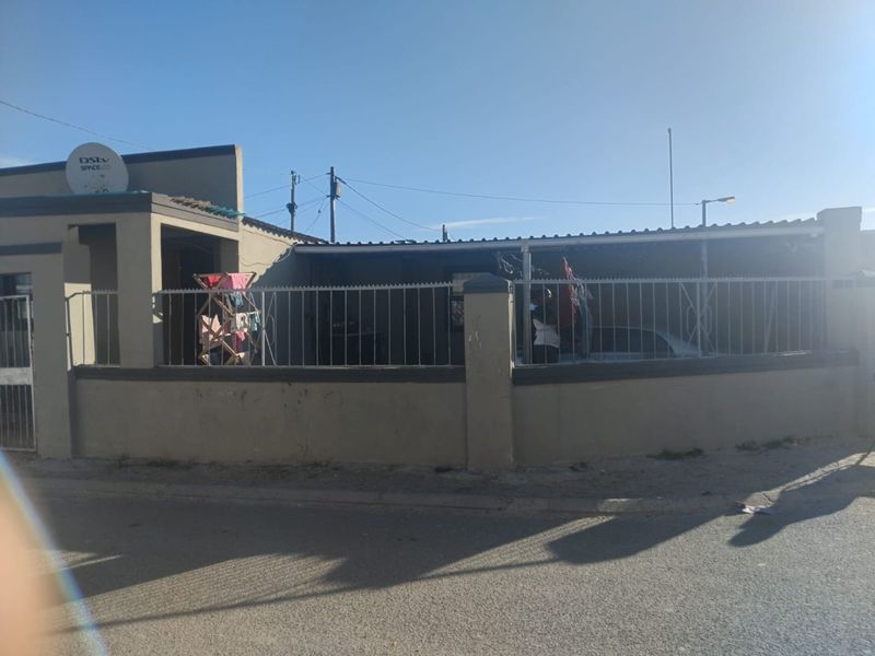 Front exterior view of a residential property featuring a perimeter wall with steel palisade fencing and a corrugated metal roof.