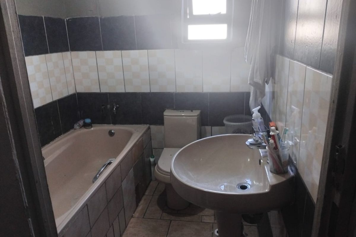 A dated bathroom featuring a bathtub, pedestal basin, and toilet with contrasting wall tiling and a small window for natural light.