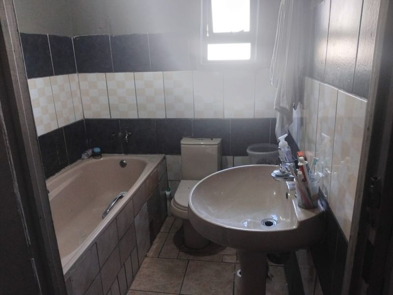 A dated bathroom featuring a bathtub, pedestal basin, and toilet with contrasting wall tiling and a small window for natural light.