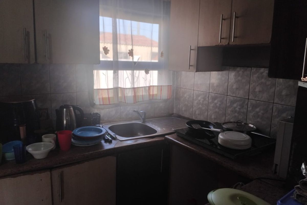A compact kitchen featuring laminate countertops, a stainless steel sink, tiled backsplash, and built-in cabinetry with an integrated electric hob.