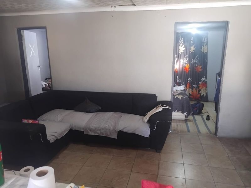 A living room area featuring tiled flooring and access to adjacent rooms, requiring cosmetic updates to improve the overall finish and appeal.