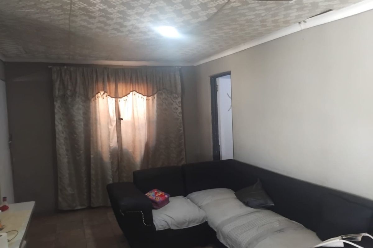 A living room area featuring tiled flooring and a textured ceiling, currently showing signs of wear and ceiling damage.