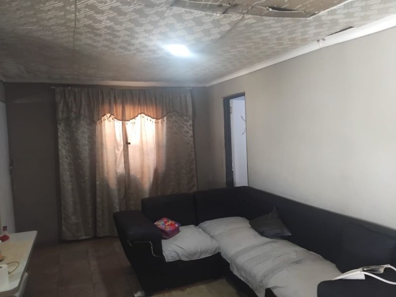 A living room area featuring tiled flooring and a textured ceiling, currently showing signs of wear and ceiling damage.