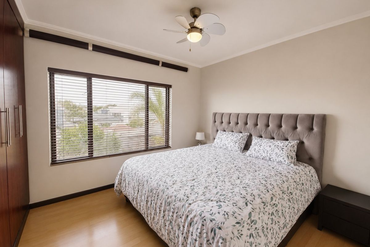 A well-maintained bedroom featuring laminate flooring, built-in cupboards, a ceiling fan, and large windows with venetian blinds.
