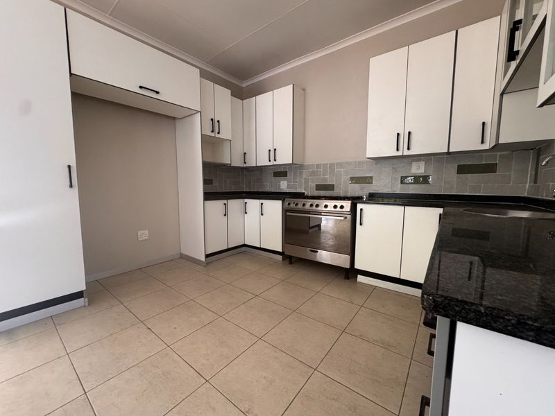 A clean, functional kitchen featuring white cabinetry, dark granite countertops, a stainless steel stove, and neutral tiled flooring.