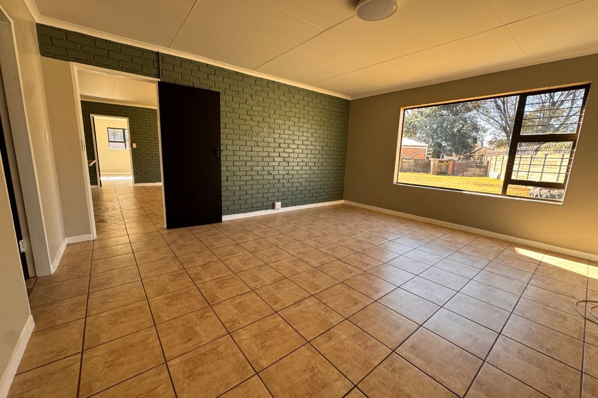 Spacious living area featuring tiled flooring, an exposed brick feature wall, and a large window providing natural light and garden views.