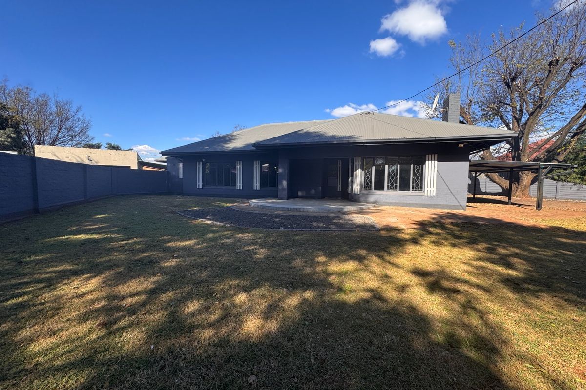 Rear view of the house featuring a dark grey painted brick facade, metal roofing, a concrete patio area, and a large enclosed garden.