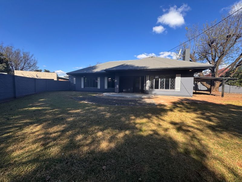 Rear view of the house featuring a dark grey painted brick facade, metal roofing, a concrete patio area, and a large enclosed garden.