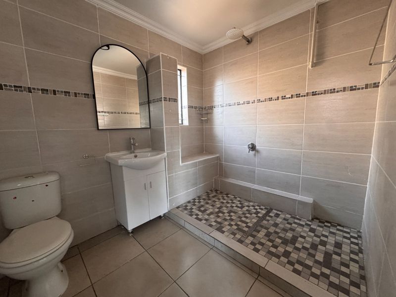 A functional bathroom featuring a walk-in shower with mosaic floor tiles, a vanity unit with basin, and neutral wall tiling throughout.