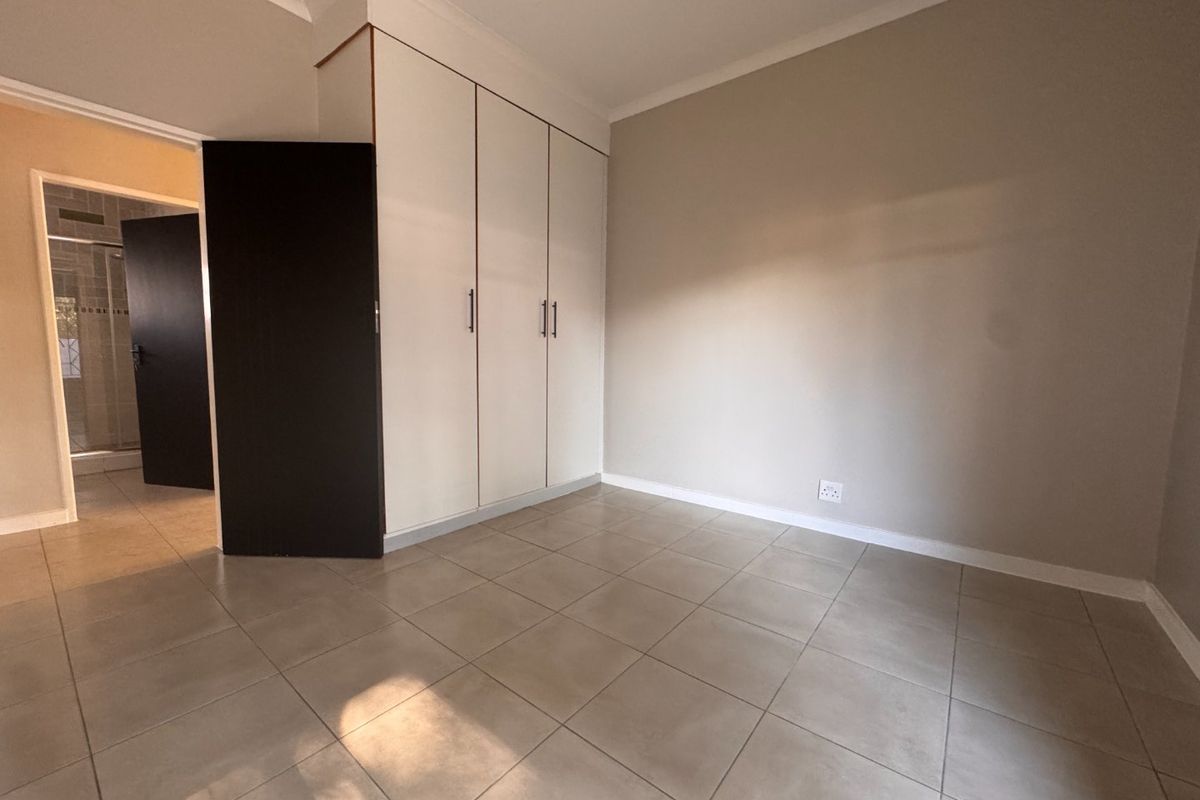A clean, empty bedroom featuring neutral tiled flooring, built-in cupboards, and coved cornicing, offering a blank canvas for personalization.