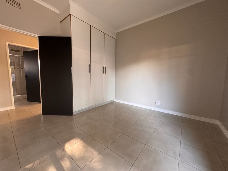 A clean, empty bedroom featuring neutral tiled flooring, built-in cupboards, and coved cornicing, offering a blank canvas for personalization.