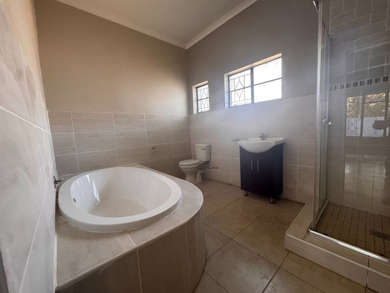 A spacious, empty bathroom featuring a built-in bathtub, separate shower enclosure, vanity cabinet with basin, and neutral wall and floor tiling.