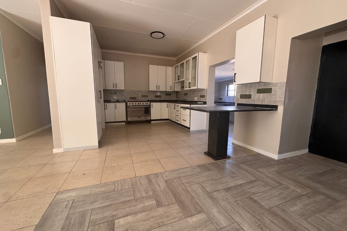 A spacious, empty kitchen featuring white cabinetry, a breakfast bar, tiled backsplash, and a mix of ceramic and laminate flooring.