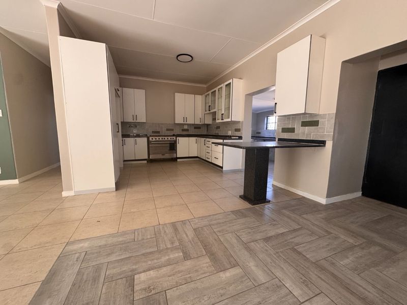 A spacious, empty kitchen featuring white cabinetry, a breakfast bar, tiled backsplash, and a mix of ceramic and laminate flooring.