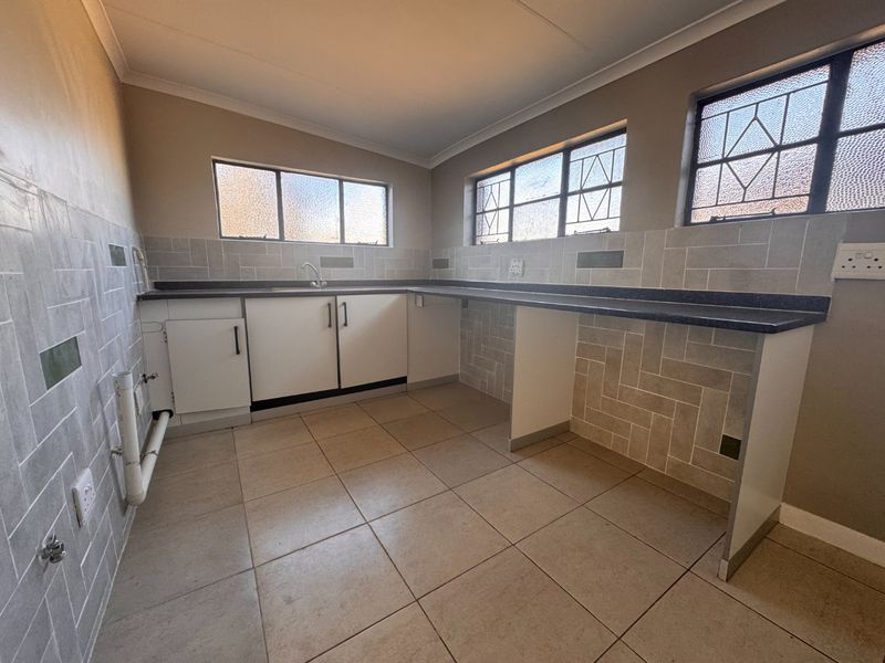 A functional scullery or laundry area featuring tiled splashbacks, laminate countertops, a stainless steel sink, and dedicated plumbing connections.