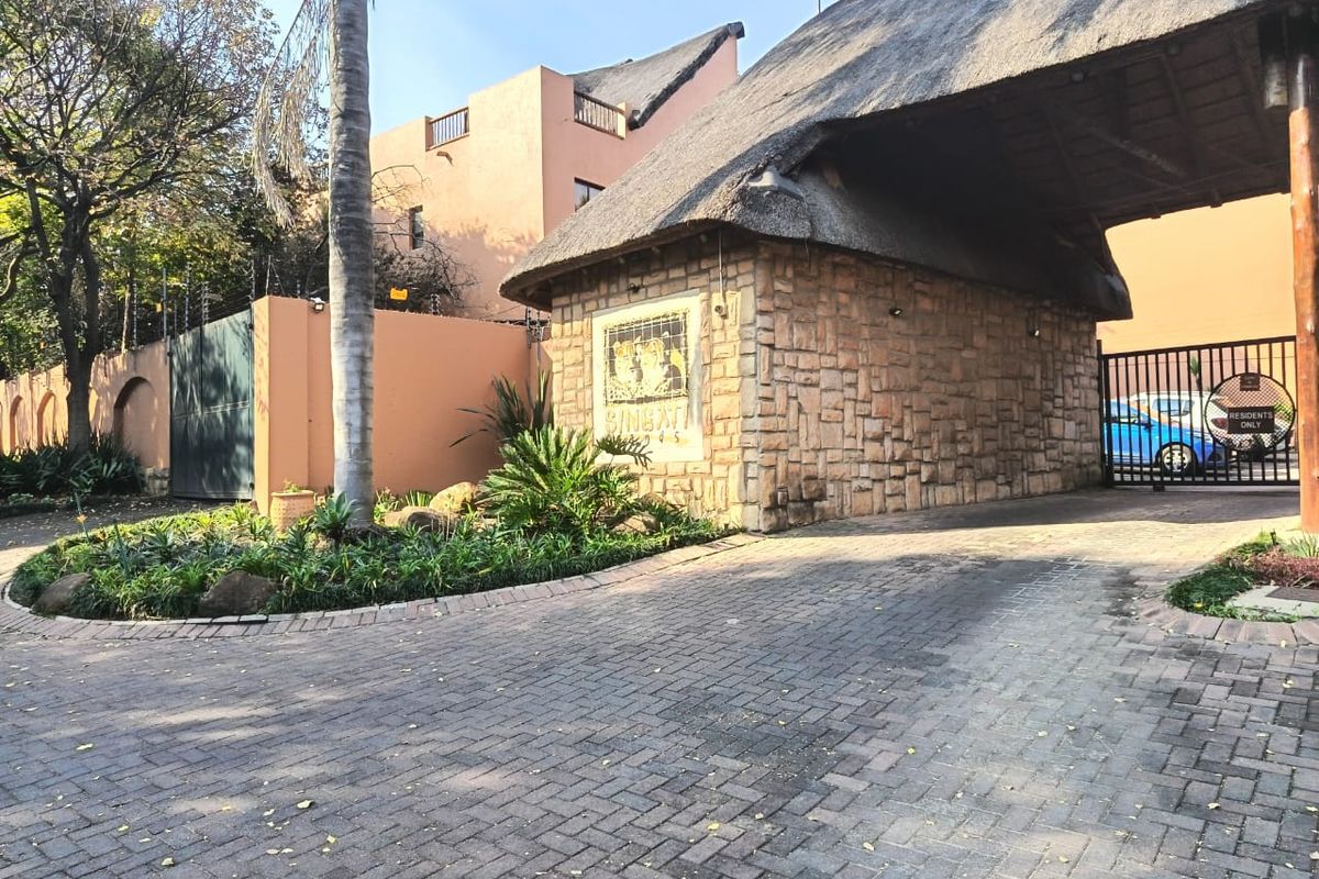 The entrance to the apartment complex features a stone-clad guardhouse with a thatched roof, paved driveway, and secure gated access.