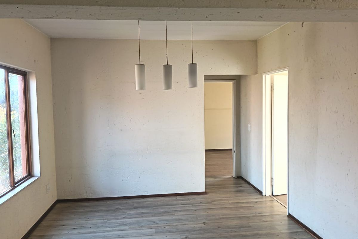 An empty living area featuring laminate flooring, an exposed ceiling beam, and modern pendant lighting, ready for personalization.