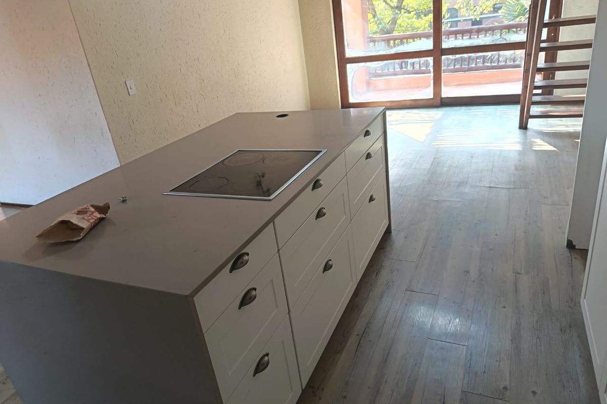 Modern kitchen island featuring a built-in electric hob, set within an open-plan living space with wood-look flooring and access to a balcony.