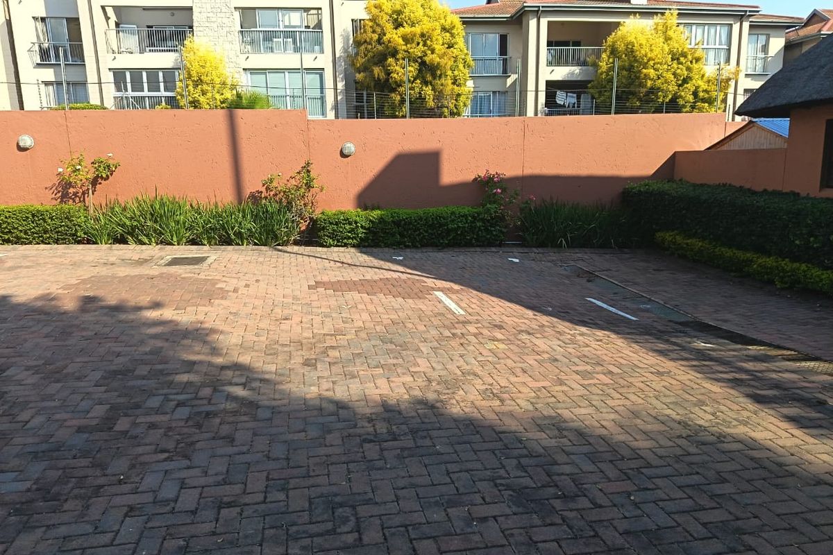 A paved parking area featuring a boundary wall with integrated lighting and established garden beds, situated within an apartment complex.