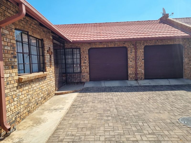 Front exterior view of a face brick house featuring a double garage, paved driveway, and secure metal window frames.