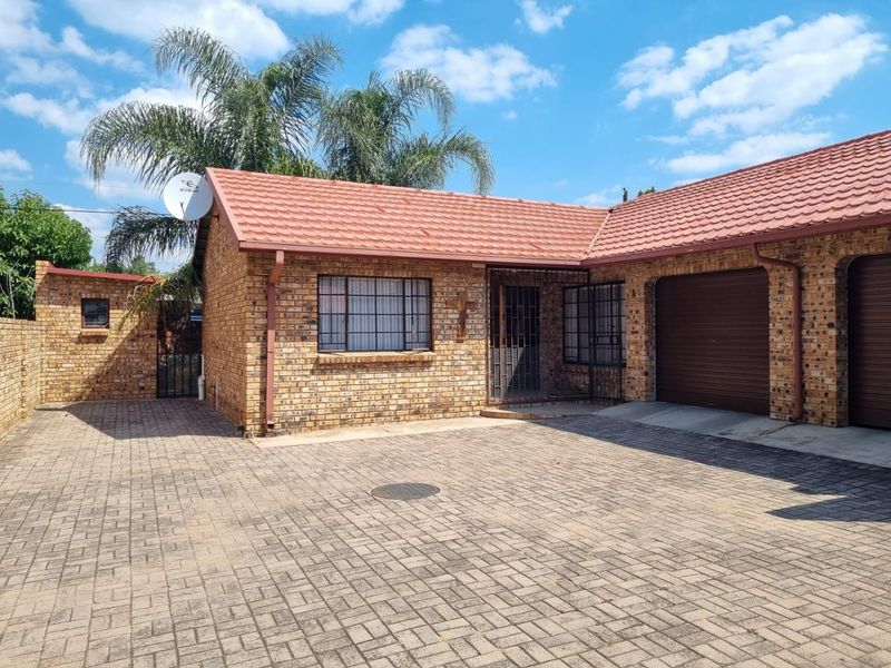 Front view of a facebrick house featuring a paved driveway, tiled roof, and secure garage access.