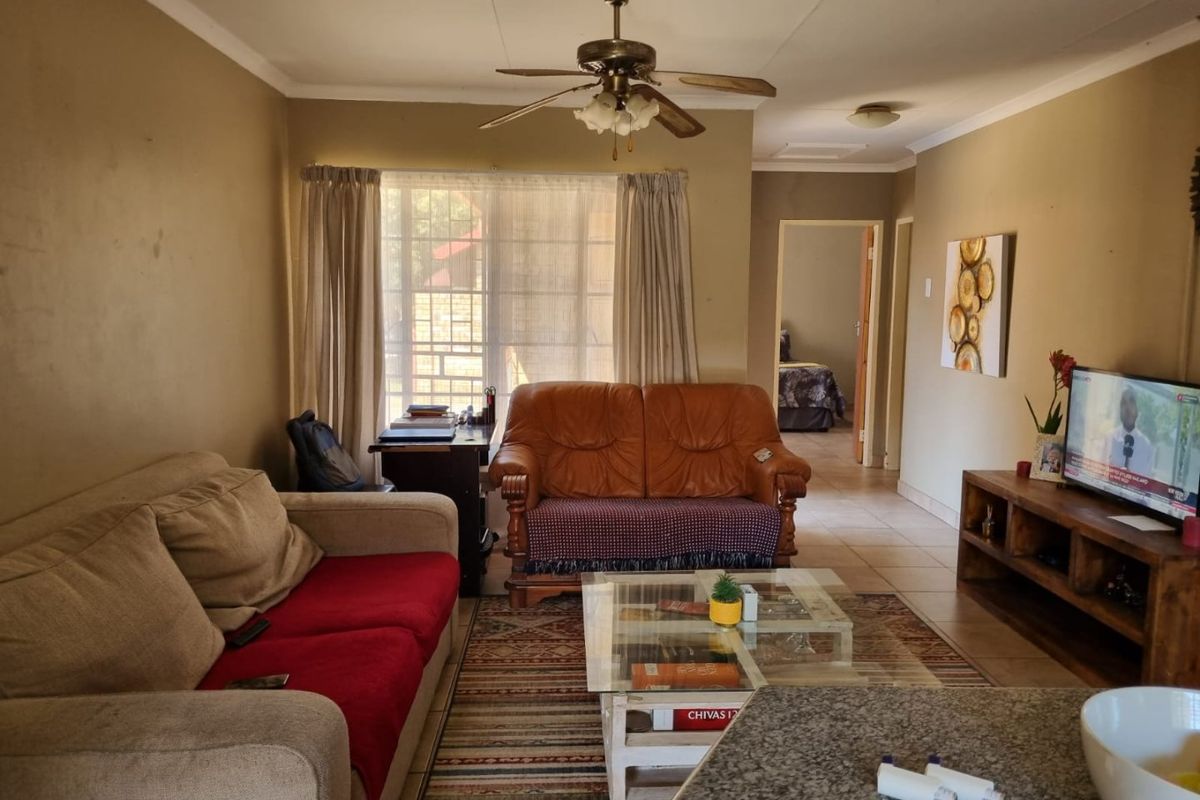 A living room featuring tiled flooring, a ceiling fan, and natural light through a window with security bars.