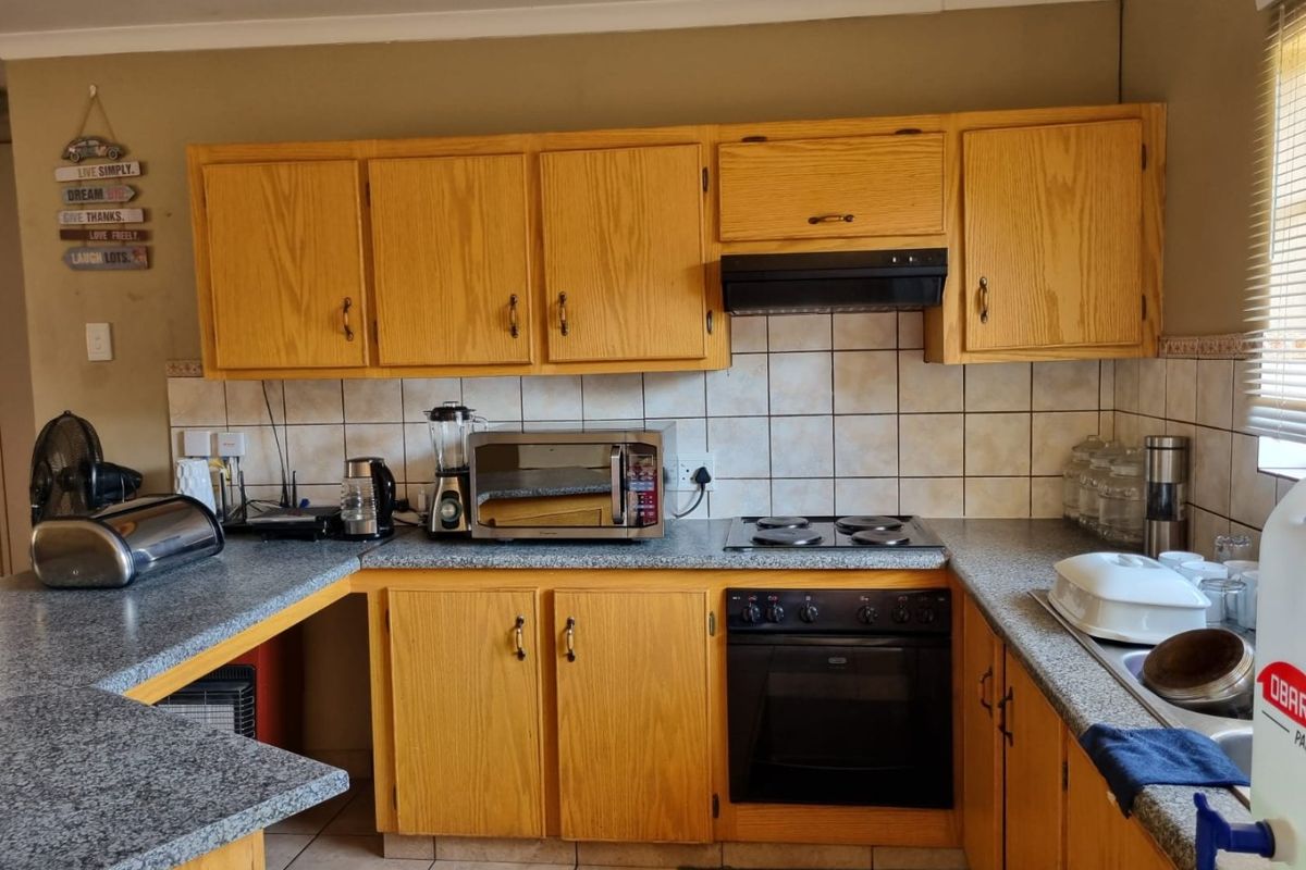 A functional kitchen featuring wooden cabinetry, laminate countertops, a built-in oven, and an electric hob with a tiled backsplash.