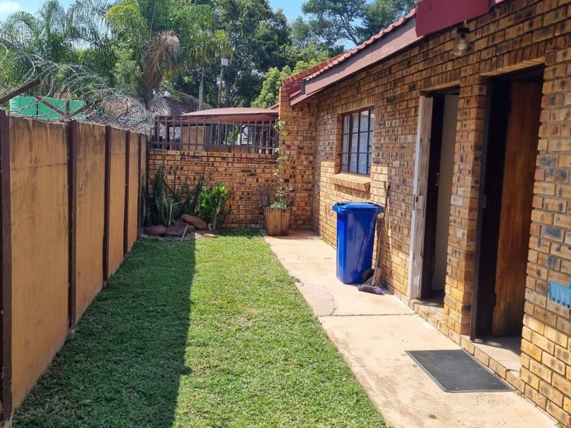A side view of the property featuring a face brick exterior, concrete pathway, and a small lawn area enclosed by a boundary wall.