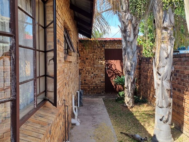 A side exterior view of the property featuring face brick walls, steel window frames, and a concrete pathway leading to a rear door.