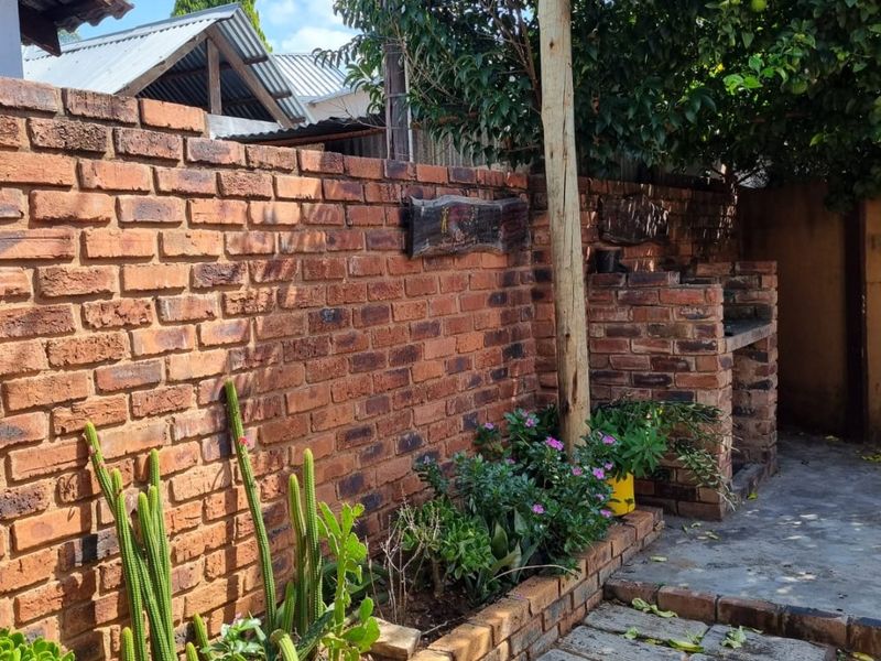 Outdoor patio area featuring a built-in brick braai, exposed brick boundary wall, and paved flooring with a raised garden planter.