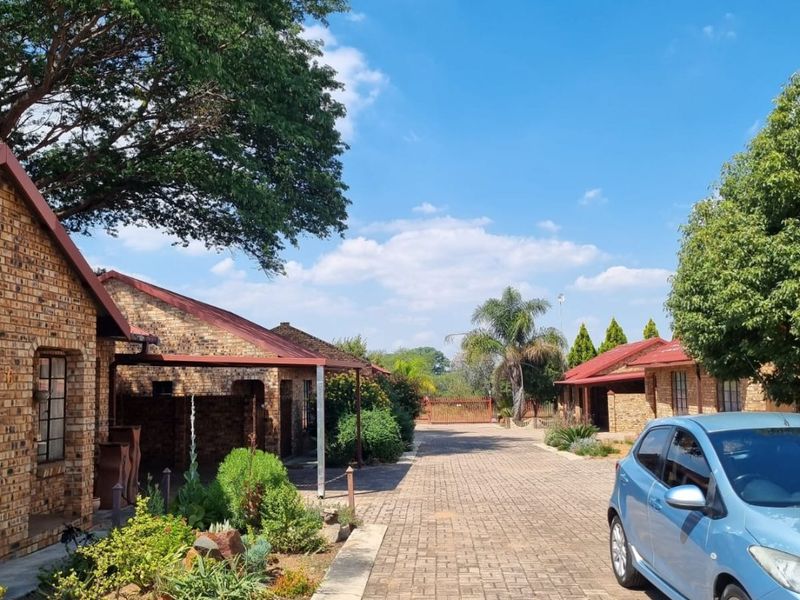 A view of the property entrance featuring a paved driveway, face brick buildings with metal roofing, and established garden landscaping.
