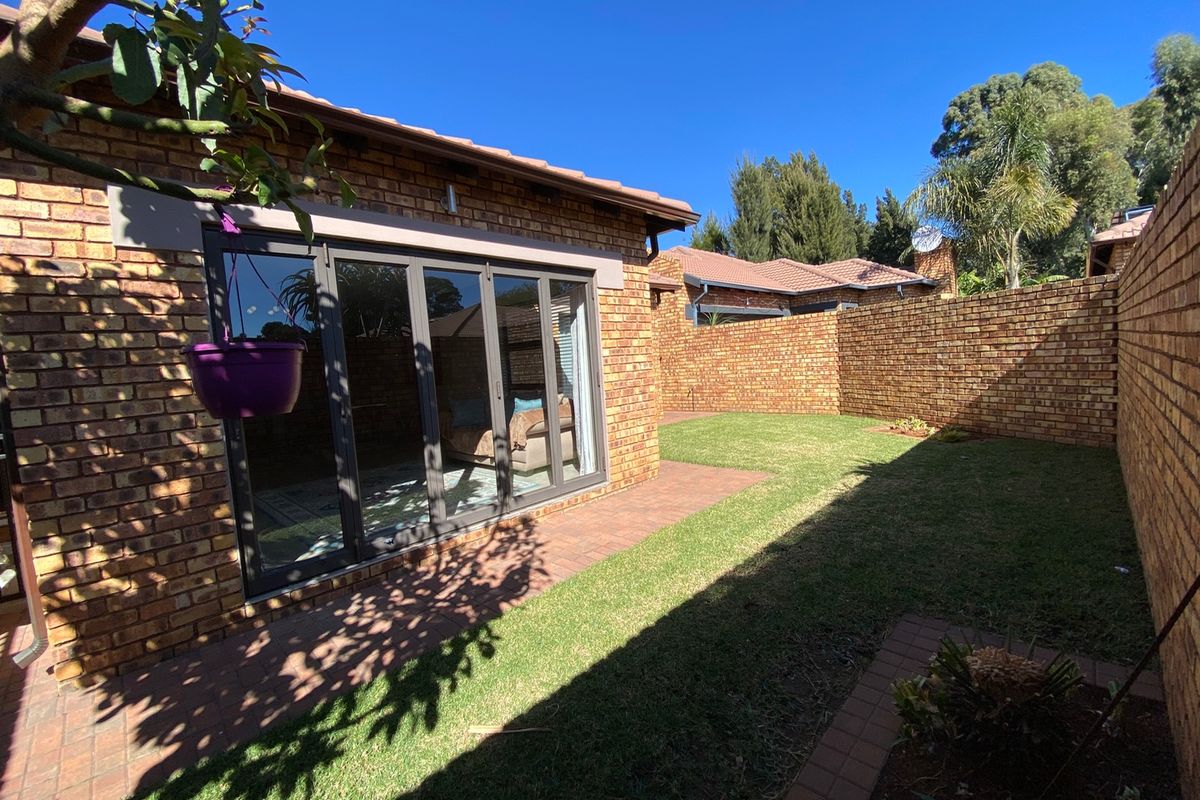 A private rear garden featuring a paved patio area, well-maintained lawn, and face brick boundary walls, accessible via modern aluminium stacker doors.