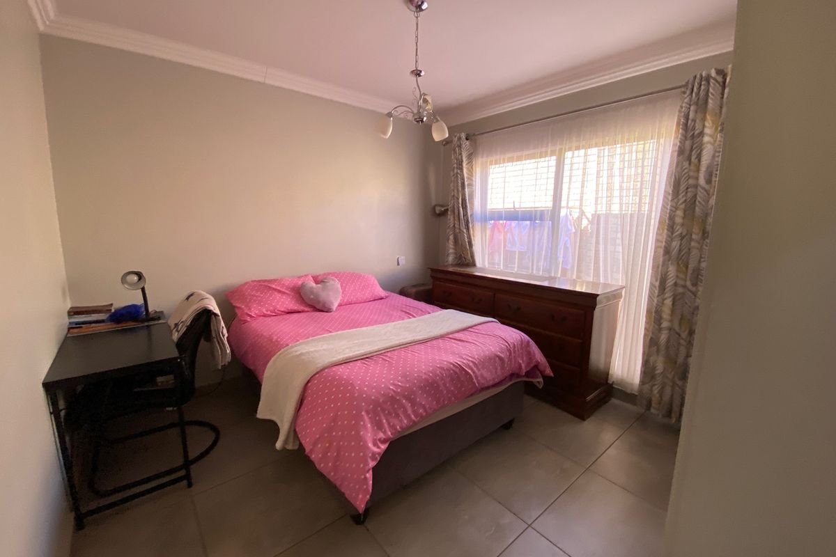 A functional bedroom featuring tiled flooring, ceiling cornice detailing, and a central pendant light fixture, providing a neutral base for personalization.