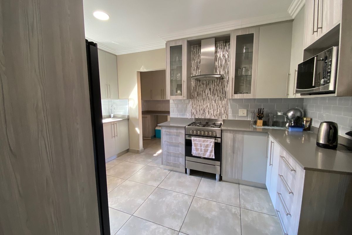 Modern kitchen featuring light wood-grain cabinetry, stone countertops, stainless steel gas stove, extractor fan, and a convenient adjoining scullery area.