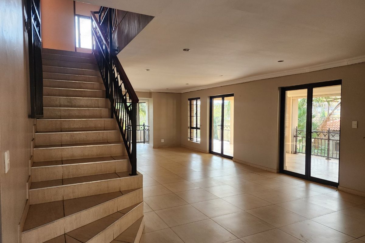 Spacious open-plan living area featuring a tiled staircase with wrought iron balustrade, large sliding glass doors, and neutral tiled flooring throughout.