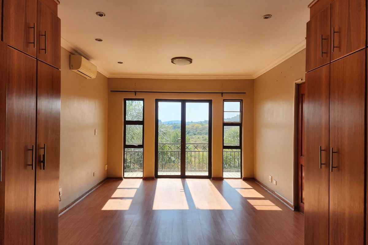 Spacious bedroom featuring built-in wooden cupboards, laminate flooring, air conditioning, and sliding doors opening onto a balcony with scenic views.