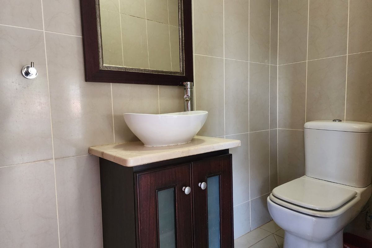 A well-maintained bathroom featuring a modern vessel sink on a stone-topped vanity cabinet, complemented by neutral wall tiling and a framed mirror.