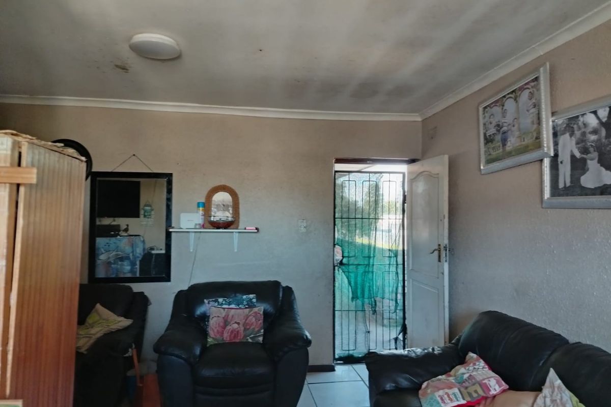 A living room area featuring tiled flooring and a security gate entrance, currently showing signs of wear and ceiling water damage.