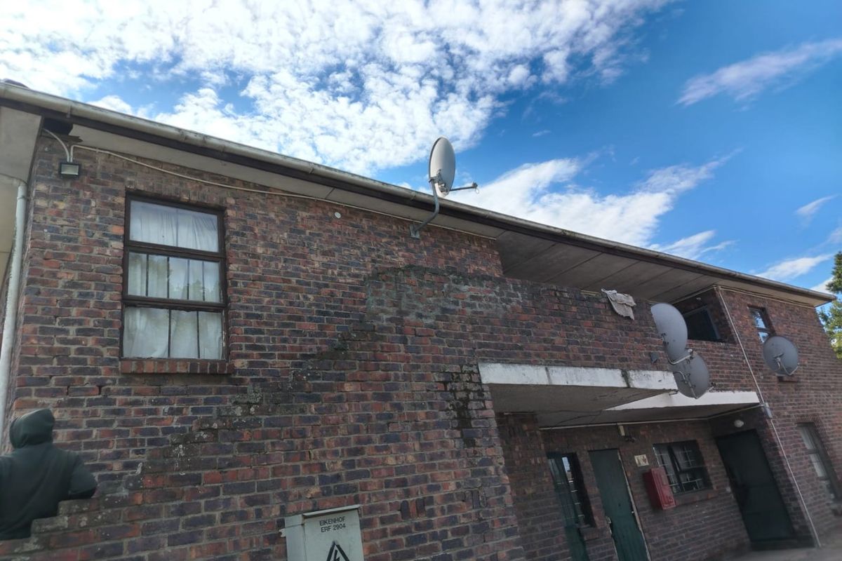 Exterior view of a brick apartment building featuring multiple satellite dishes, exposed brickwork, and a concrete balcony structure.
