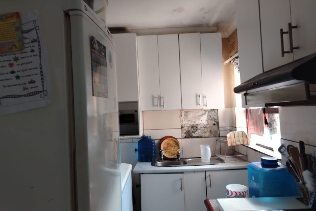 Compact kitchen featuring white cabinetry, stainless steel sink, and extractor fan, currently showing signs of significant wear and water damage to walls and ceiling.