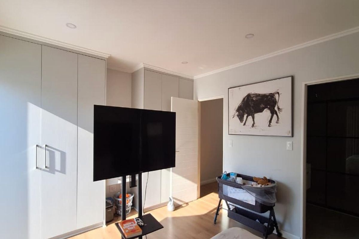 A well-maintained bedroom featuring neutral walls, laminate flooring, recessed downlighting, and ample built-in cupboard storage.