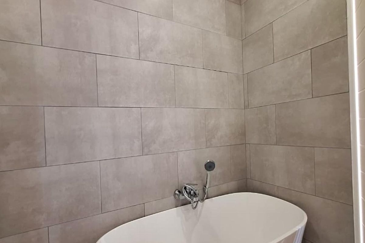 Modern bathroom featuring a clean freestanding bathtub with wall-mounted chrome fixtures and contemporary grey ceramic wall tiles.