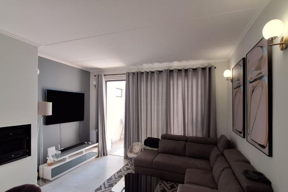 A well-maintained living room featuring a built-in fireplace, modern wall lighting, tiled floors, and direct access to an outdoor patio area.